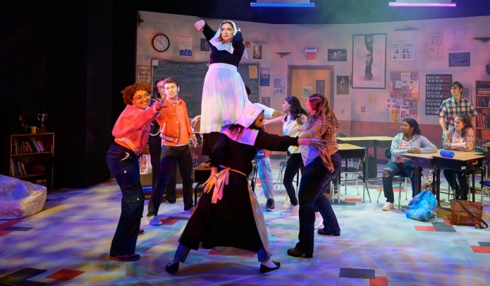 Student in Puritan costume dances on a school desk while several other individuals dance around her