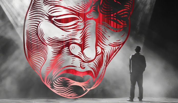 Man stands alone on stage with a shroud of light and an ominous red drama mask looms over him